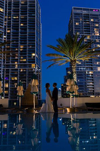 A couple stands hand in hand in front of the EPIC pool at dusk.