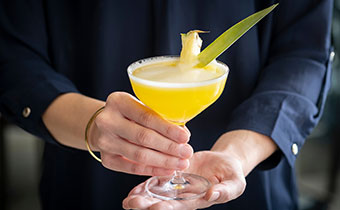 A yellow cocktail with pineapple leaf garnish